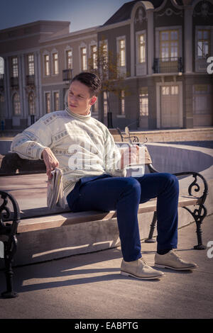 L'homme avec des lunettes en blanc pour homme de l'emplacement sur le banc et holding newspaper à côté de fontaine en ville et à la recherche de côté Banque D'Images