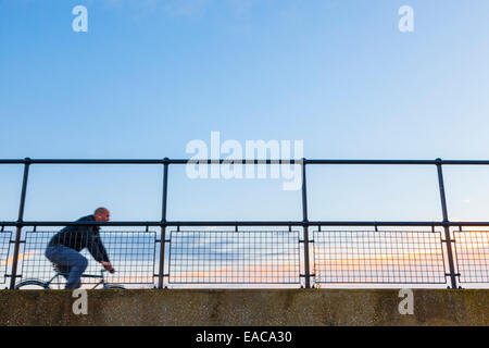 À la recherche jusqu'à un cycliste vélo sur un pont, passage contre un ciel du soir, England, UK Banque D'Images