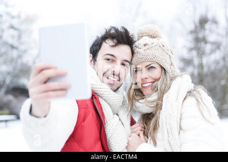 Couple heureux en hiver à prendre des photos d'eux-mêmes avec tablet PC Banque D'Images