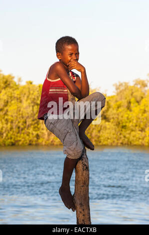 Garçon malgache assis sur un poteau, Morondava, la province de Toliara, Madagascar Banque D'Images