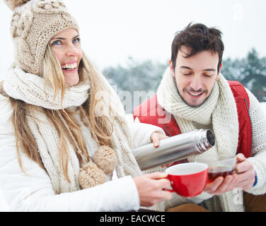 Happy woman pouring homme plateau de thermos en hiver Banque D'Images