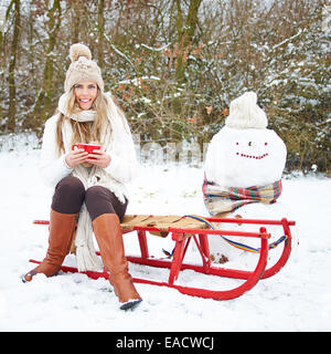 Smiling woman sitting avec plateau en hiver sur un traîneau à côté d'un bonhomme Banque D'Images