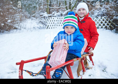 Deux enfants tenant leurs cadeaux de Noël sur un traîneau en hiver Banque D'Images