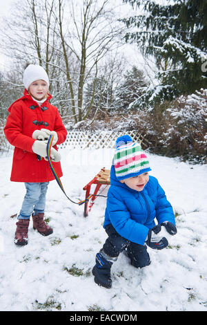 Deux enfants avec un traîneau jouent dans la neige en hiver Banque D'Images