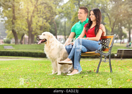 Jeune couple assis dans un parc avec un chien sur un banc en bois Banque D'Images