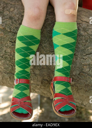 Fille avec pansement sur le genou, avec des chaussettes et des sandales assis sur un grand arbre branche Banque D'Images