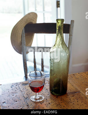 Bouteille vide et verre de vin rouge par porte ouverte avec chapeau de paille se reposant sur une chaise Banque D'Images