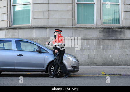 Un gardien de la circulation émet un ticket de parking pour une voiture en stationnement illégal. Banque D'Images