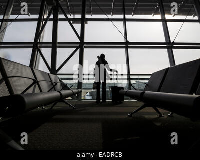 Silhouette d'une personne avec une valise de matériel roulant en face d'une fenêtre de terminal de l'aéroport Banque D'Images