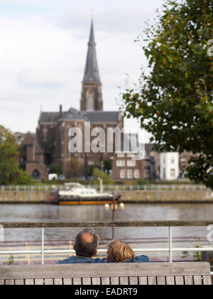 Couple d'âge moyen sur un banc de parc en face de la Meuse et la tour de l'église Saint Martin à Maastricht, Pays-Bas Banque D'Images