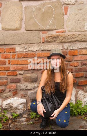 Jolie jeune fille assise contre un mur dans la rue de la vieille ville. Banque D'Images