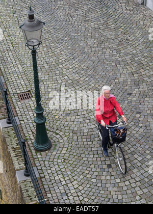 Vue de dessus d'une vieille dame de rouler à vélo dans une rue pavée Banque D'Images