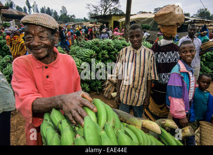 Smiling farmer la vente de bananes à cuire, regarder les passants curieux marché Mwika le marché de la banane, la région de Kilimandjaro, Tanzanie Banque D'Images