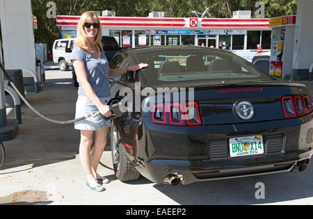 Femme automobiliste dans une station d'essence un remplissage Ford Mustang noir voiture de sport en France Banque D'Images