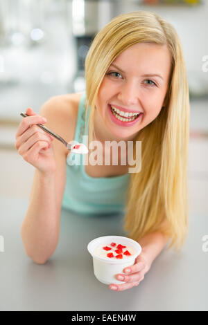 Happy young woman eating yogurt in kitchen Banque D'Images