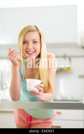 Happy young woman eating yogurt in kitchen Banque D'Images