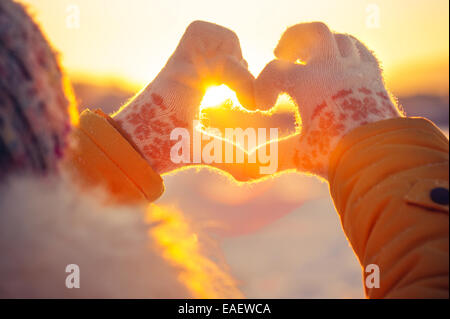 Femme les mains dans des gants d'hiver en forme de symbole du coeur et des sentiments de vie concept avec coucher du soleil lumière nature sur l'arrière-plan Banque D'Images