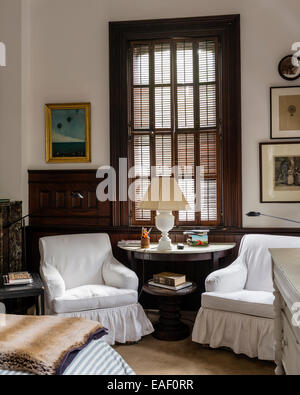 Paire de fauteuils profonds avec un accompagnement feuillets coton demilune table dans chambre avec volets d'origine Banque D'Images