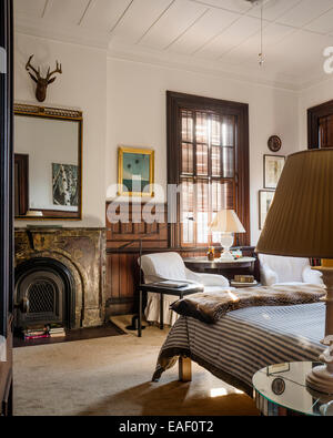 Paire de fauteuils profonds avec un accompagnement feuillets coton demilune table dans une chambre avec cheminée et des volets d'origine Banque D'Images