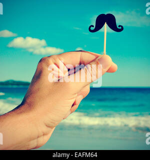 Homme d'une main tenant un fake moustache dans un bâton dans sa main sur la plage, avec un effet de filtre Banque D'Images