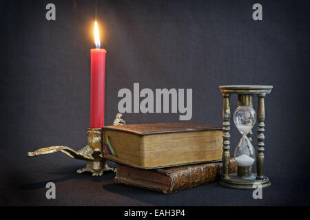 Vintage Books et hourglass sur fond sombre avec bougie rouge feu Banque D'Images