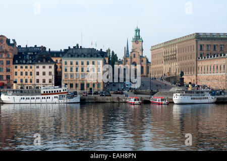 Des bateaux amarrés bordent un front de mer historique de Stockholm sous une tour de l'horloge, l'église Saint-Nicolas (Storkyrkan) vue depuis le pont Skeppsholm, Stockholm, Banque D'Images
