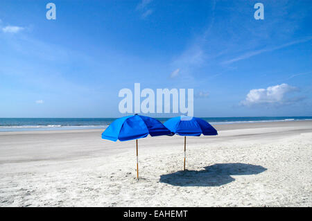 Parasol : deux parasols de plage sont placés sur la plage en face d'un beau ciel bleu avec des nuages. Banque D'Images