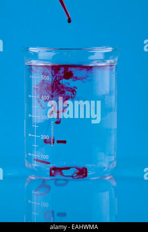 Colorant alimentaire rouge tombé dans un bécher d'eau. Banque D'Images