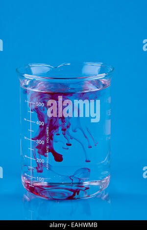 Colorant alimentaire rouge tombé dans un bécher d'eau. Banque D'Images