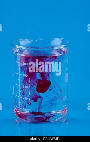 Colorant alimentaire rouge tombé dans un bécher d'eau. Banque D'Images