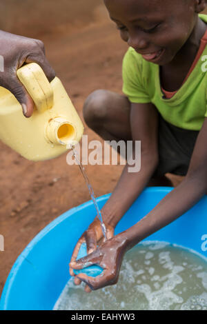 Un garçon se lave les mains avec l'aide d'un travailleur communautaire - Bukwo, District de l'Ouganda, l'Afrique de l'Est. Banque D'Images