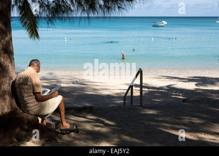 L'Ile Maurice, Pereybere, public, plage, homme assis, lisant le journal à l'ombre Banque D'Images