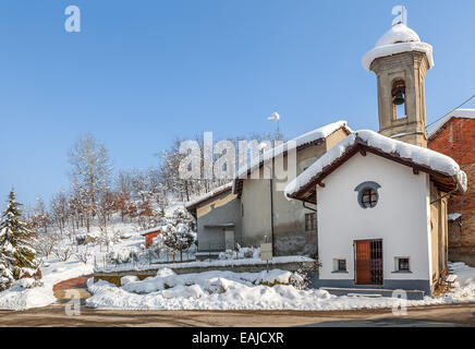 Petite chapelle rurale couverte de neige blanche sous ciel bleu ensoleillé en journée d'hiver de Piémont, Italie du Nord. Banque D'Images