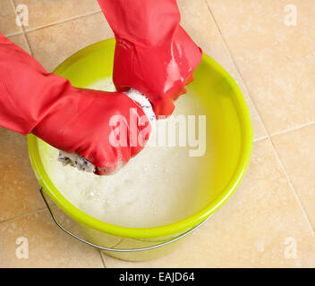 Les mains dans les gants en caoutchouc rouge essorage de l'eau d'une rdp clot Banque D'Images