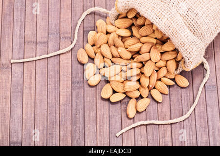 Gros plan d'amandes renversé déversés par un sac de toile, sur un fond de bois. Banque D'Images