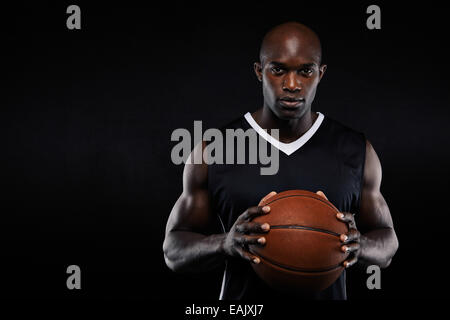 Portrait de l'Afrique de basket-ball professionnel joueur tenant une boule en regardant la caméra. Mettre en place jeune homme avec le basket-ball contre le noir Banque D'Images