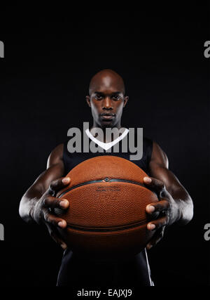 Portrait de joueur de basket-ball africain professionnel avec une balle à l'arrière-plan noir. Fit young man holding basket-ball. Banque D'Images