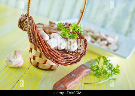 Les champignons crus en panier et sur une table Banque D'Images