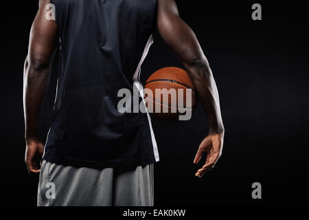 Vue arrière du joueur de basket avec un ballon dans ses bras sur fond noir avec l'exemplaire de l'espace. Banque D'Images