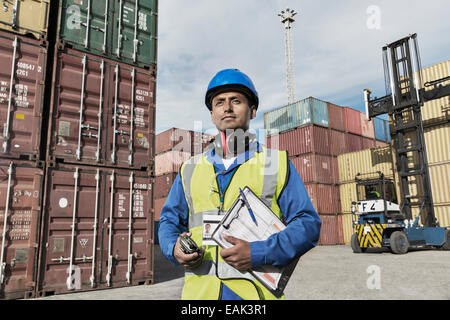 Worker holding clipboard près de conteneurs de fret Banque D'Images