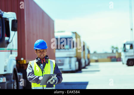 Worker using digital tablet près de camions avec les conteneurs de fret Banque D'Images