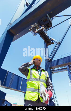 Low angle view of worker talking on talkie-walkie sous grue de chargement Banque D'Images