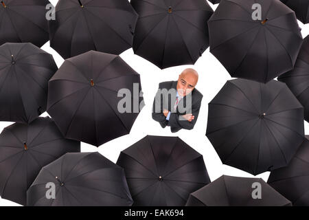 Businessman standing parmi les parapluies noir en blanc isolé Banque D'Images