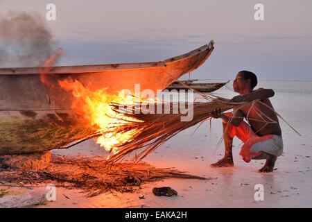 Son bateau pêcheur fumeurs à la combustion de feuilles de palmier, pour durcir la surface et d'éliminer la vermine, Dongwe Beach, Dongwe, Zanzibar Banque D'Images