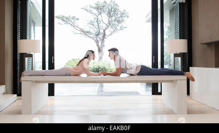 Couple lying on table face à face et se tenant la main, arbre vu à travers la porte patio en arrière-plan Banque D'Images