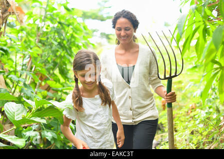 Fille et femme avec fourche de jardinage marche à travers plants in greenhouse Banque D'Images