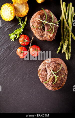 Morceaux de steaks de viande rouge avec légumes et épices, servi sur la surface de la pierre noire. Tourné à partir de la vue supérieure Banque D'Images