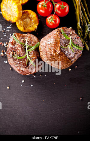 Morceaux de steaks de viande rouge avec légumes et épices, servi sur la surface de la pierre noire. Tourné à partir de la vue supérieure Banque D'Images