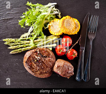 Morceaux de steaks de viande rouge avec légumes et épices, servi sur la surface de la pierre noire. Tourné à partir de la vue supérieure Banque D'Images