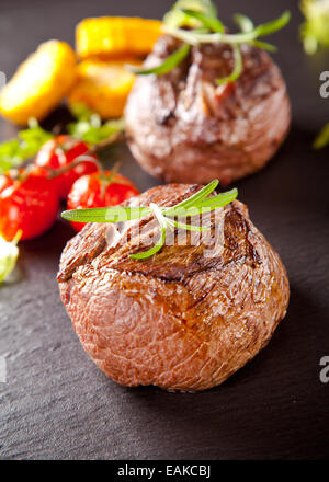 Pavé de boeuf servi avec légumes grillés et des herbes sur table en pierre noire Banque D'Images